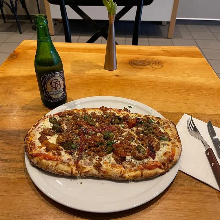 Nygräddad pinsa serverad vid bordet, med öl och en blomma i vas